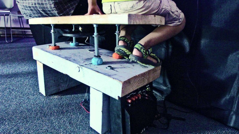 Two visitors sit on a vibro-haptic bench prototype designed at CymaSpace to feel sound and music via vibration and touch.