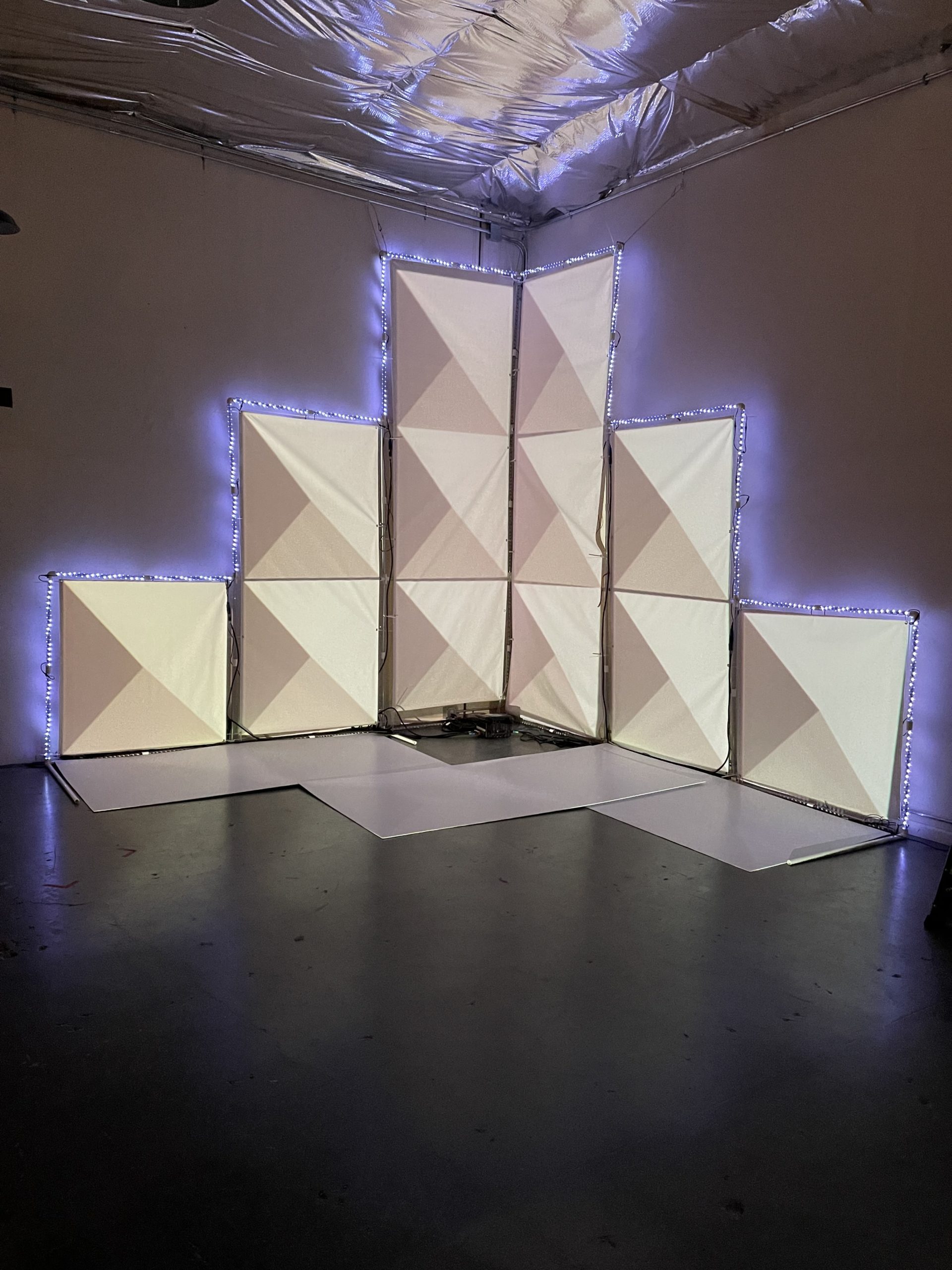 a snow white geometric pyramid structure made of squares and a 3D illusion of triangles projected onto one corner of a warehouse wall.